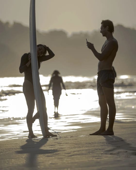 Photographer shooting a surfer holding her board on the beach at golden hour