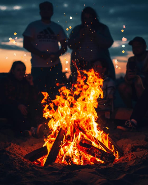 Surfers gathered around a beach bonfire at dusk in Weligama